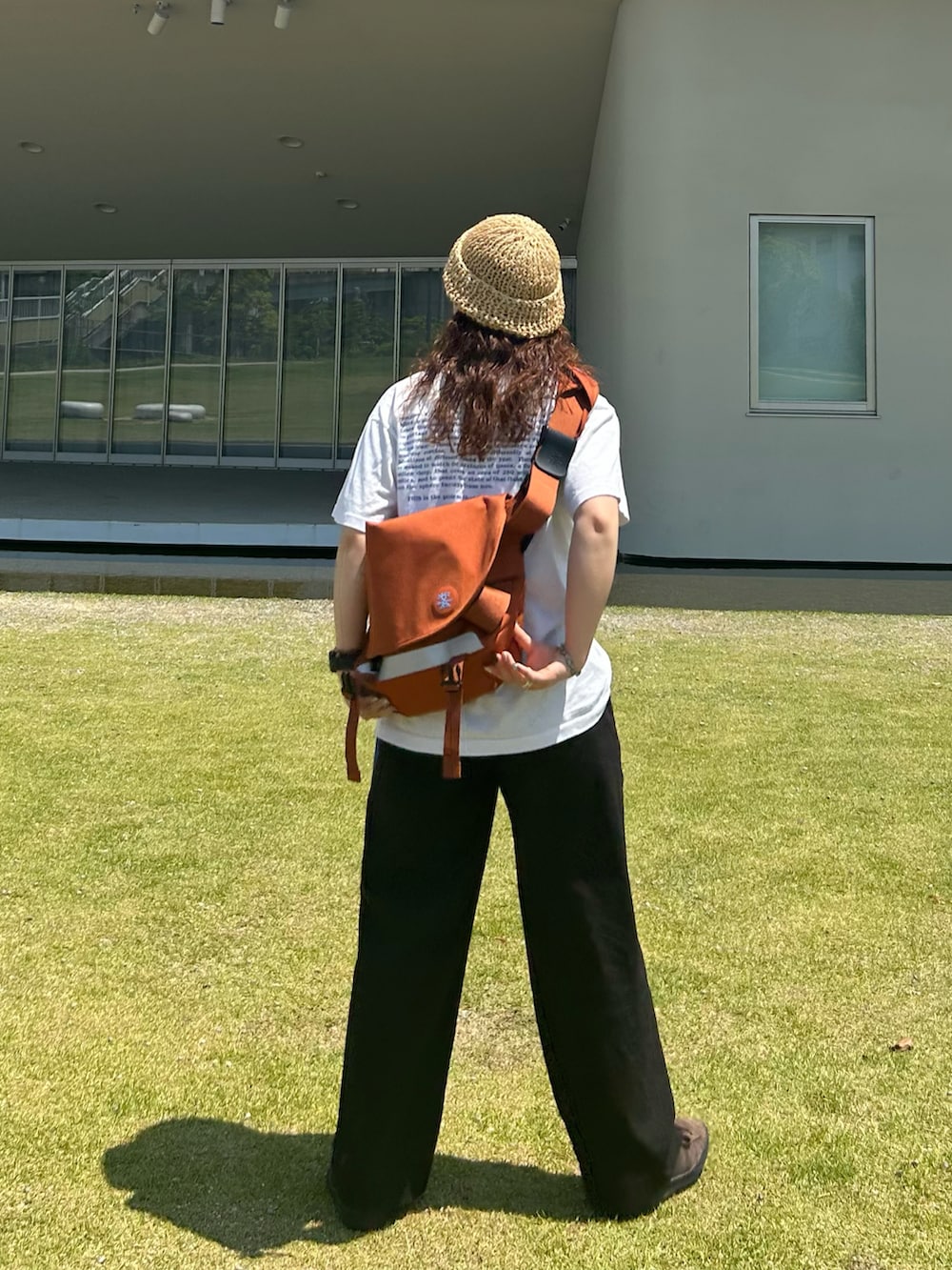 ブラック系のスラックス、ブラウン系のスニーカー、オレンジ系のメッセンジャーバッグを着用したレディースの夏コーディネートの2枚目の写真