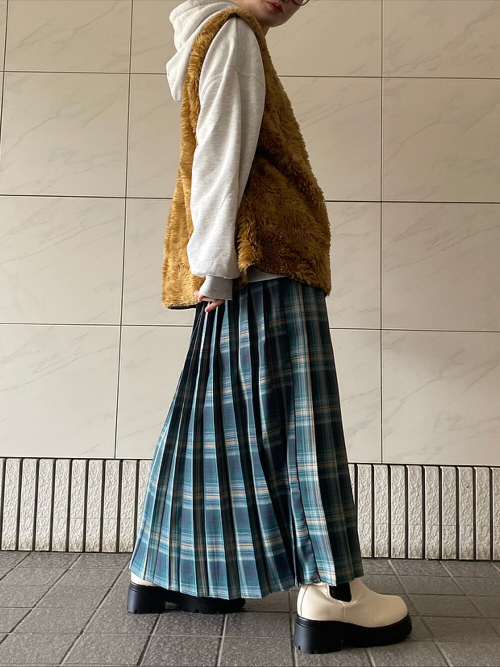 グリーン系のスカート、ホワイト系のブーツ、ブラウン系のベストを着用したレディースの冬コーディネートの2枚目の写真