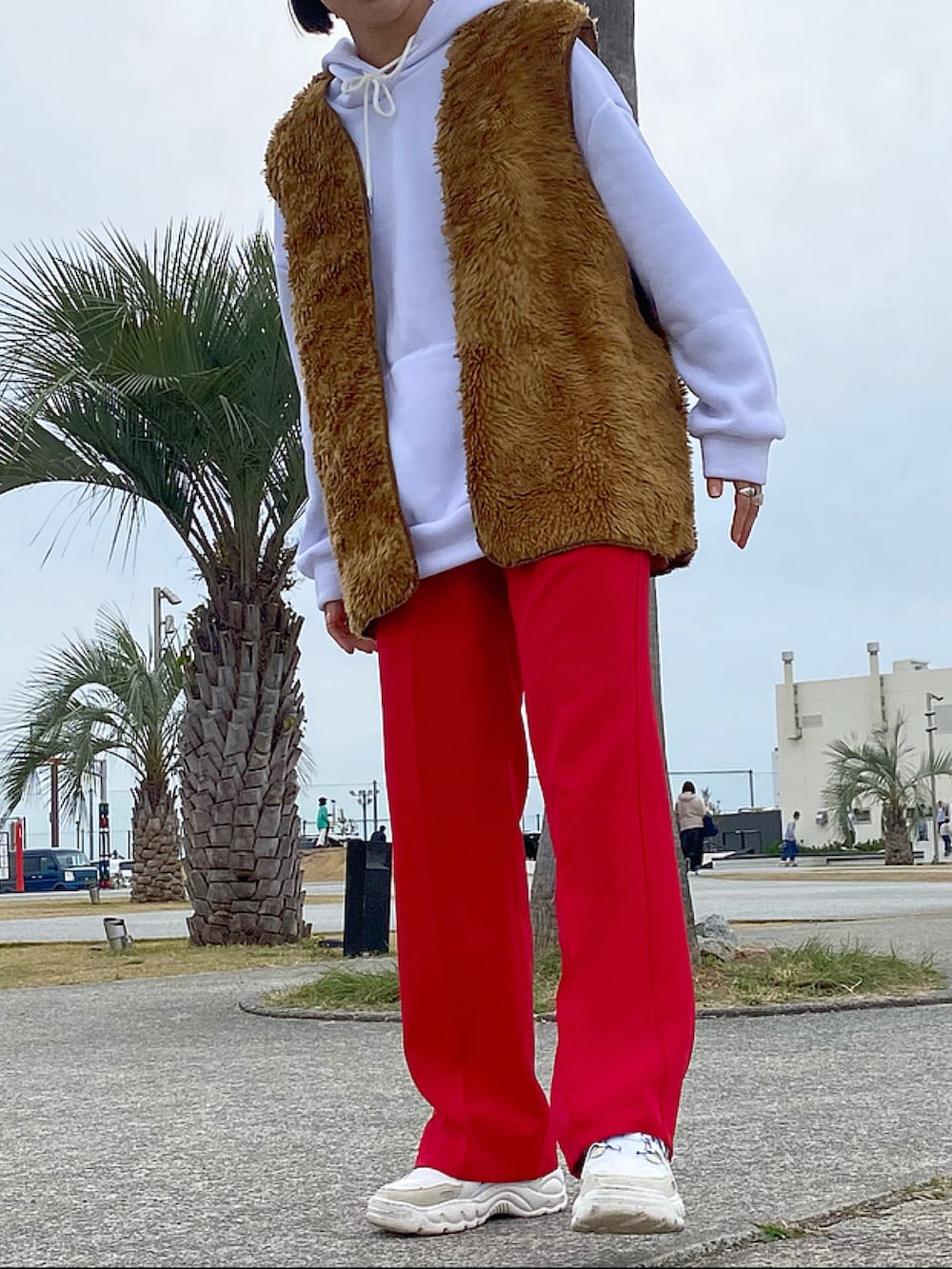 レッド系のスラックス、ホワイト系のスニーカー、ブラウン系のベストを着用したレディースの秋コーディネートの2枚目の写真