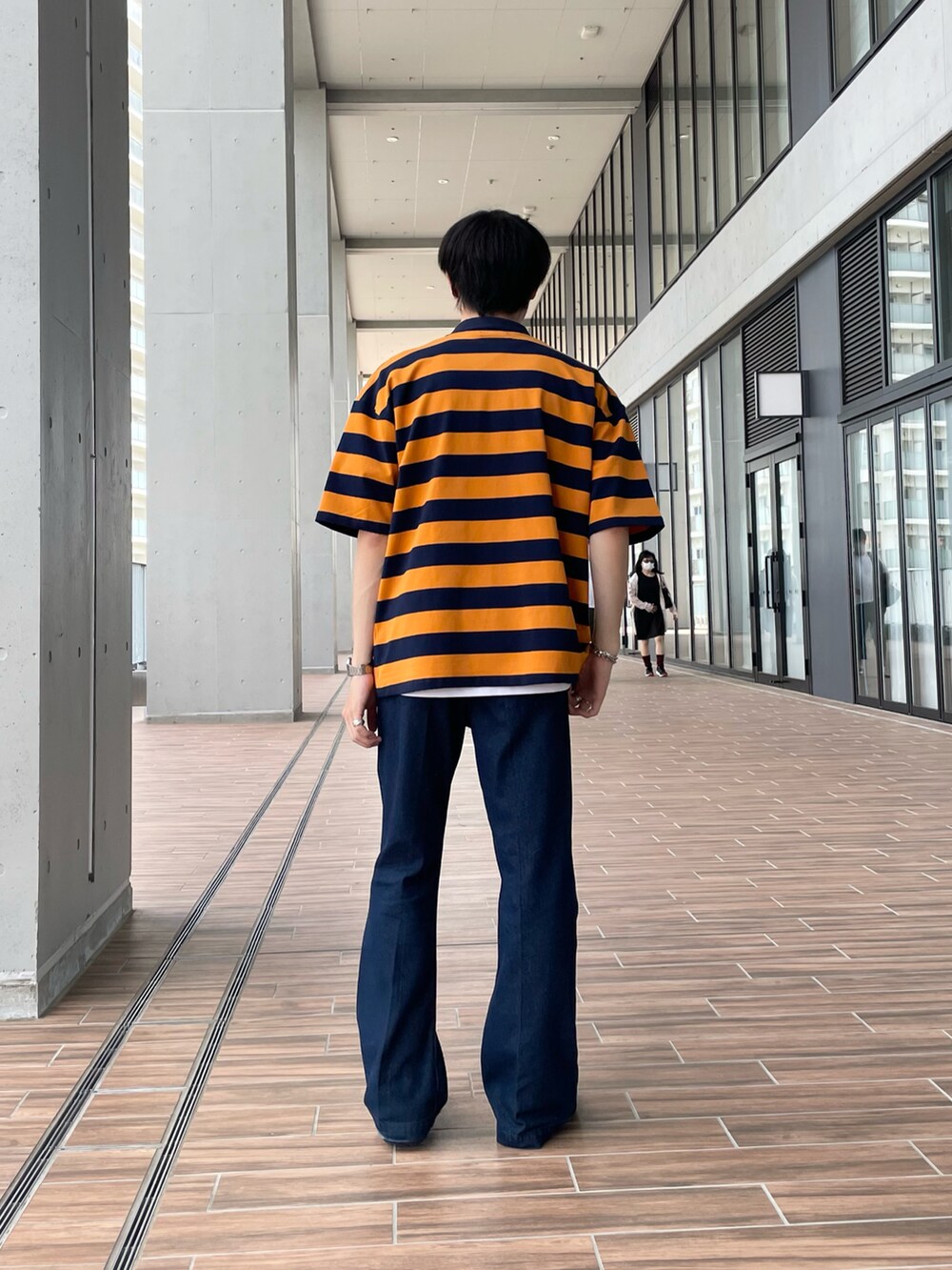 オレンジ系のポロシャツ、ブルー系のデニムパンツ、ブラック系のサンダルを着用したメンズの夏コーディネートの2枚目の写真