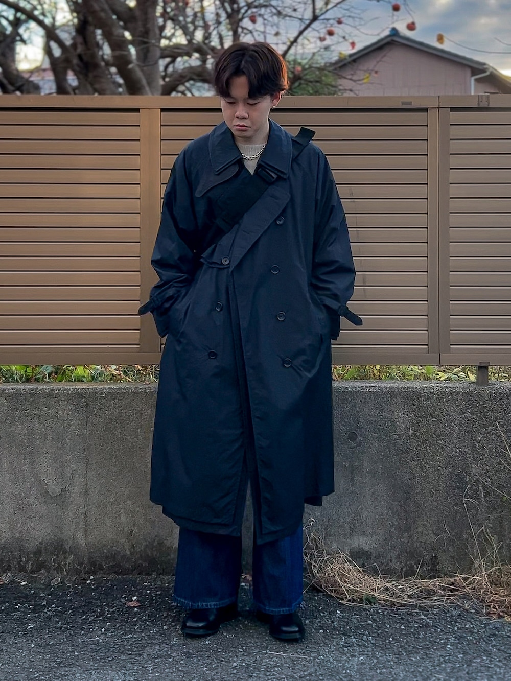 ブラック系のトレンチコート、グレー系のニット/セーター、ブルー系のデニムパンツを着用したメンズの冬コーディネートの2枚目の写真