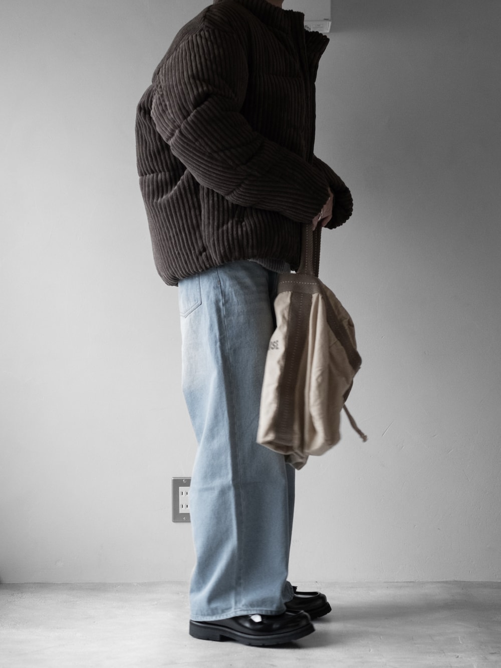 グレー系のニット/セーター、ブラウン系のダウンジャケット/コート、グリーン系のショルダーバッグを着用したメンズの秋コーディネートの3枚目の写真