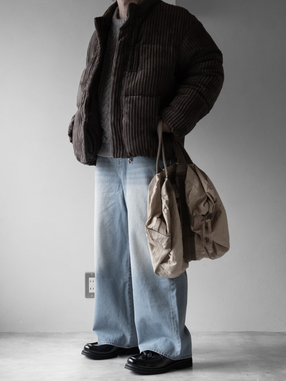 グレー系のニット/セーター、ブラウン系のダウンジャケット/コート、グリーン系のショルダーバッグを着用したメンズの秋コーディネートの2枚目の写真