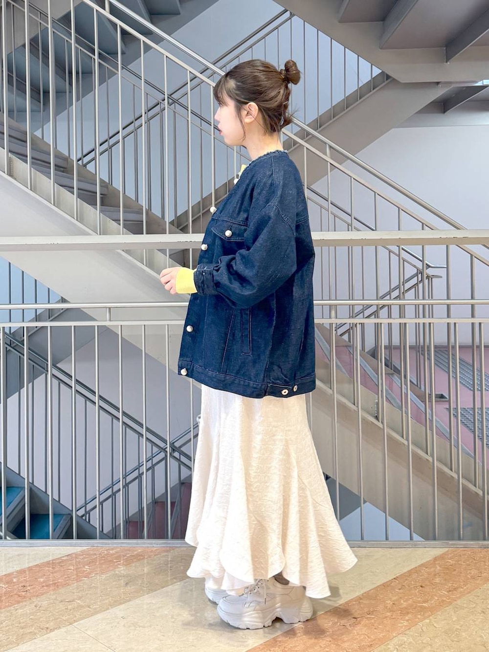 イエロー系のニット/セーター、シルバー系のハンドバッグ、ホワイト系のスニーカーを着用したレディースの春コーディネートの2枚目の写真