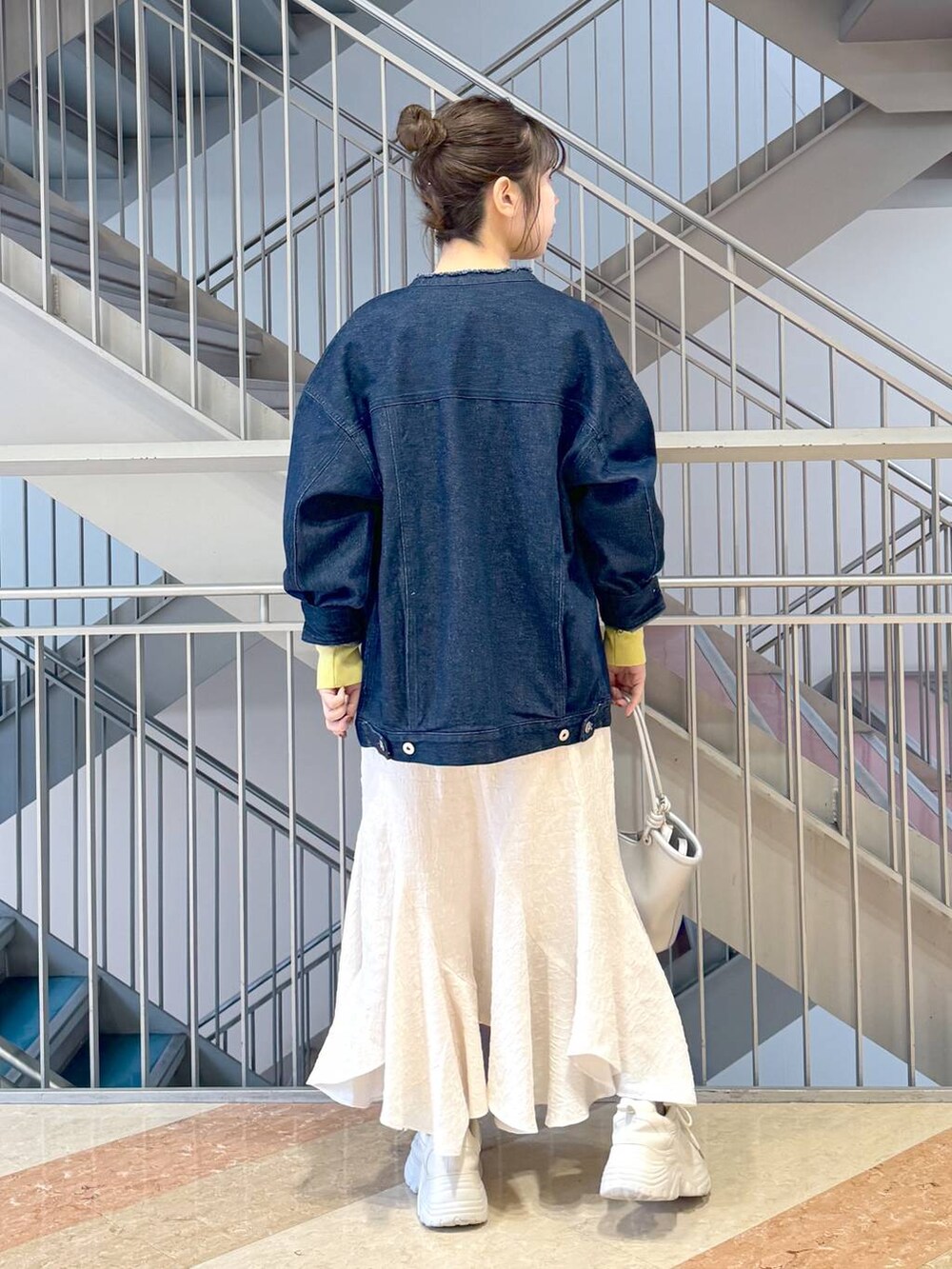 イエロー系のニット/セーター、シルバー系のハンドバッグ、ホワイト系のスニーカーを着用したレディースの春コーディネートの3枚目の写真