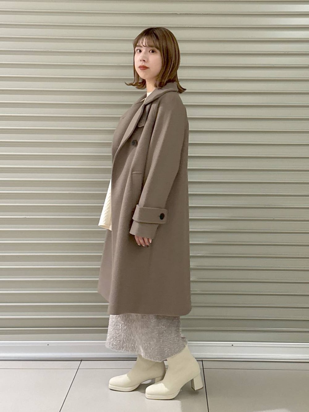 ブラウン系のチェスターコート、ホワイト系のブーツ、ホワイト系のハンドバッグを着用したレディースの冬コーディネートの3枚目の写真