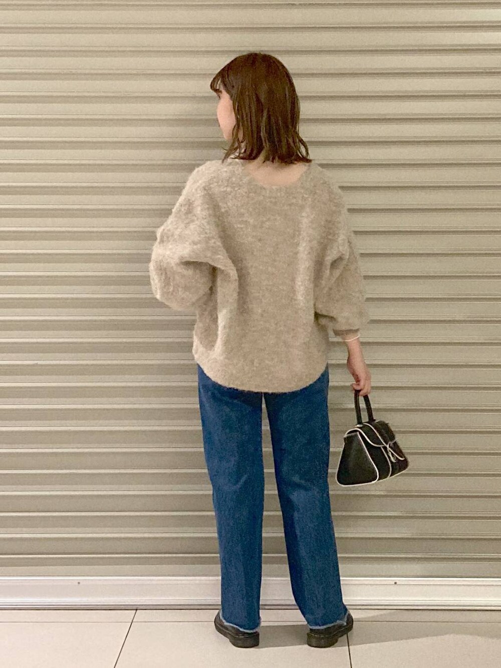 ブルー系のデニムパンツ、ブラック系のハンドバッグ、ブラウン系のカーディガン/ボレロを着用したレディースの秋コーディネートの2枚目の写真