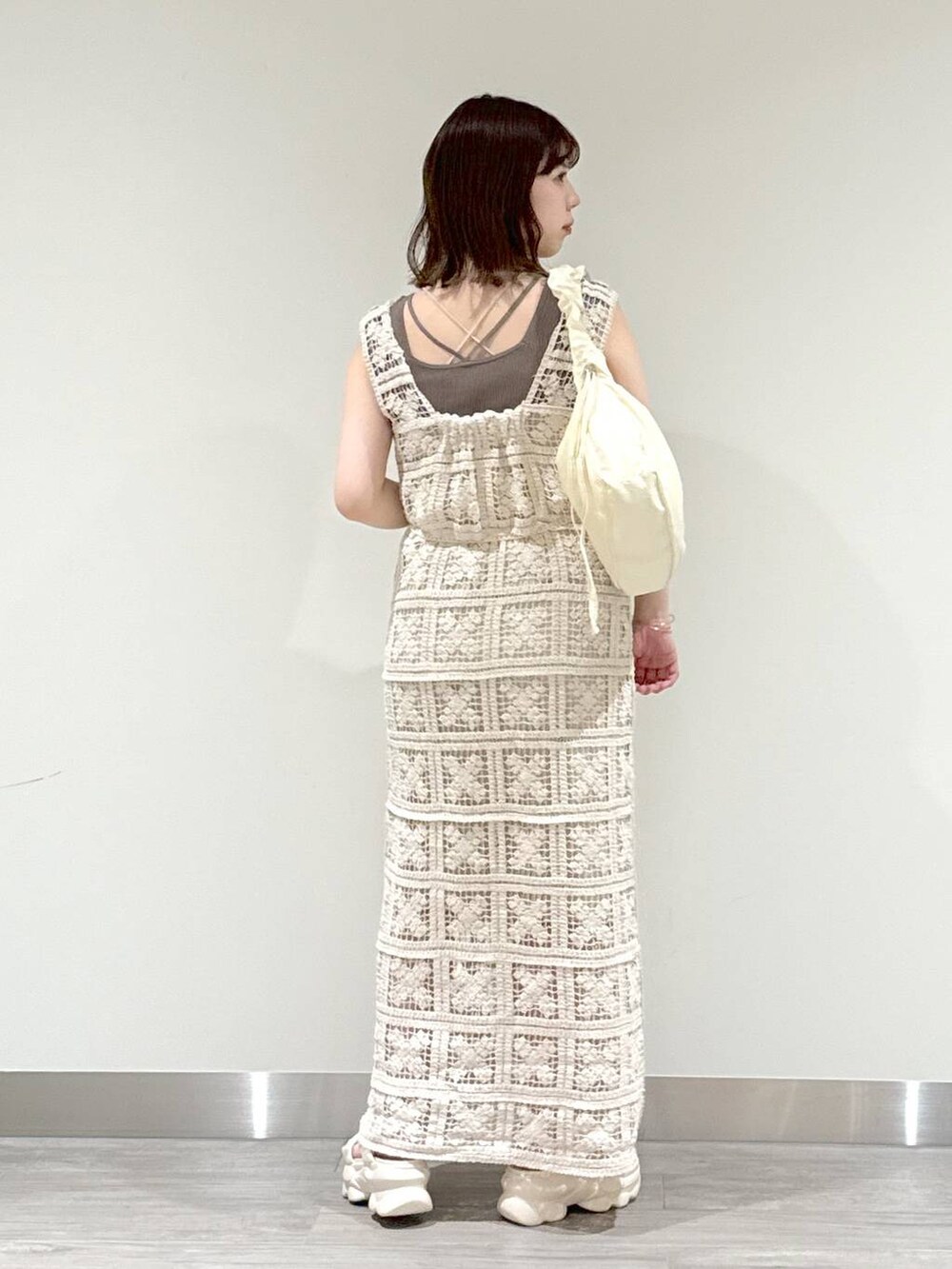 ホワイト系のワンピース、ブラウン系のニット/セーター、ホワイト系のサンダルを着用したレディースの春コーディネートの2枚目の写真