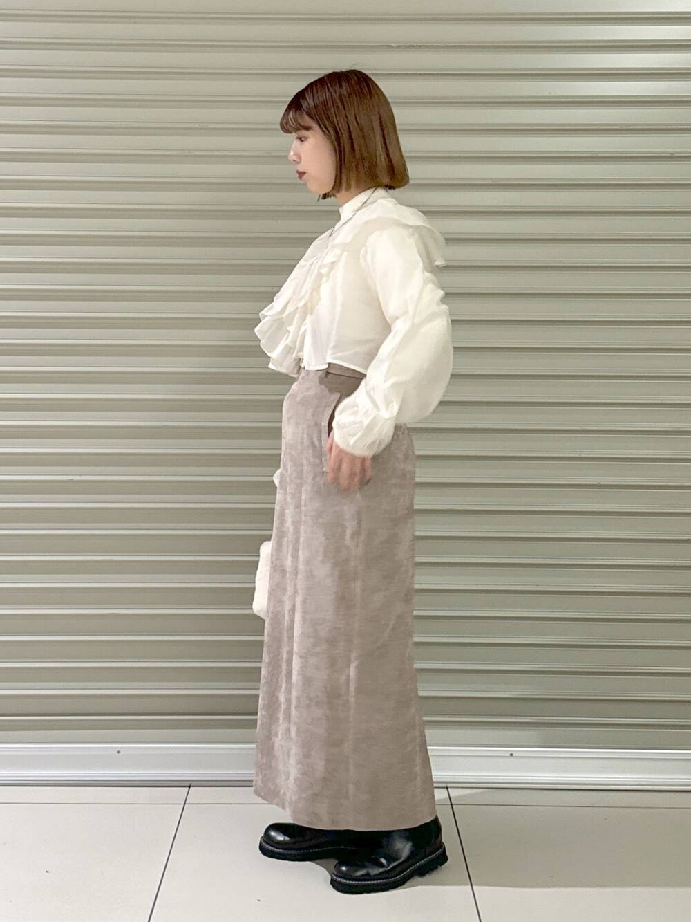 ブラウン系のスカート、ブラック系のブーツ、ホワイト系のハンドバッグを着用したレディースの冬コーディネートの2枚目の写真