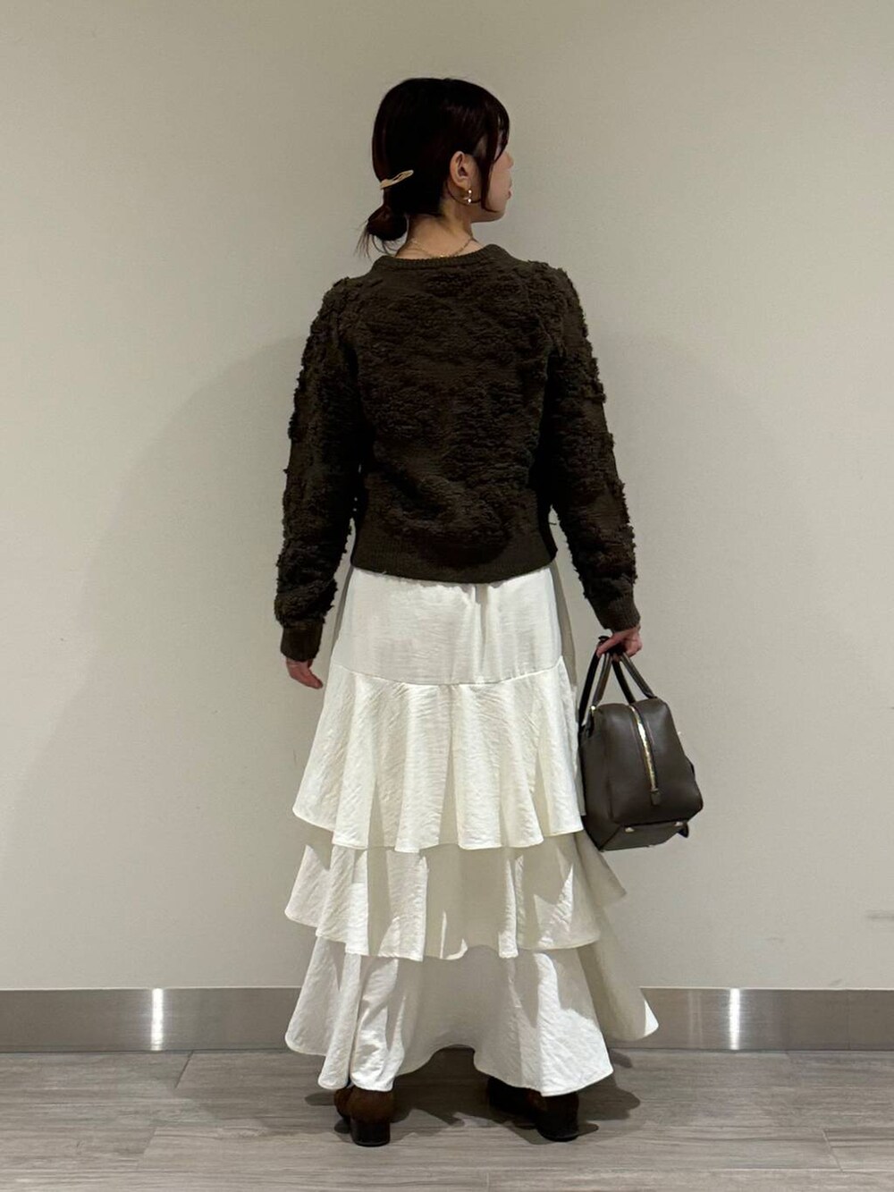 ブラウン系のハンドバッグ、ブラウン系のカーディガン/ボレロ、ホワイト系のスカートを着用したレディースの秋コーディネートの3枚目の写真