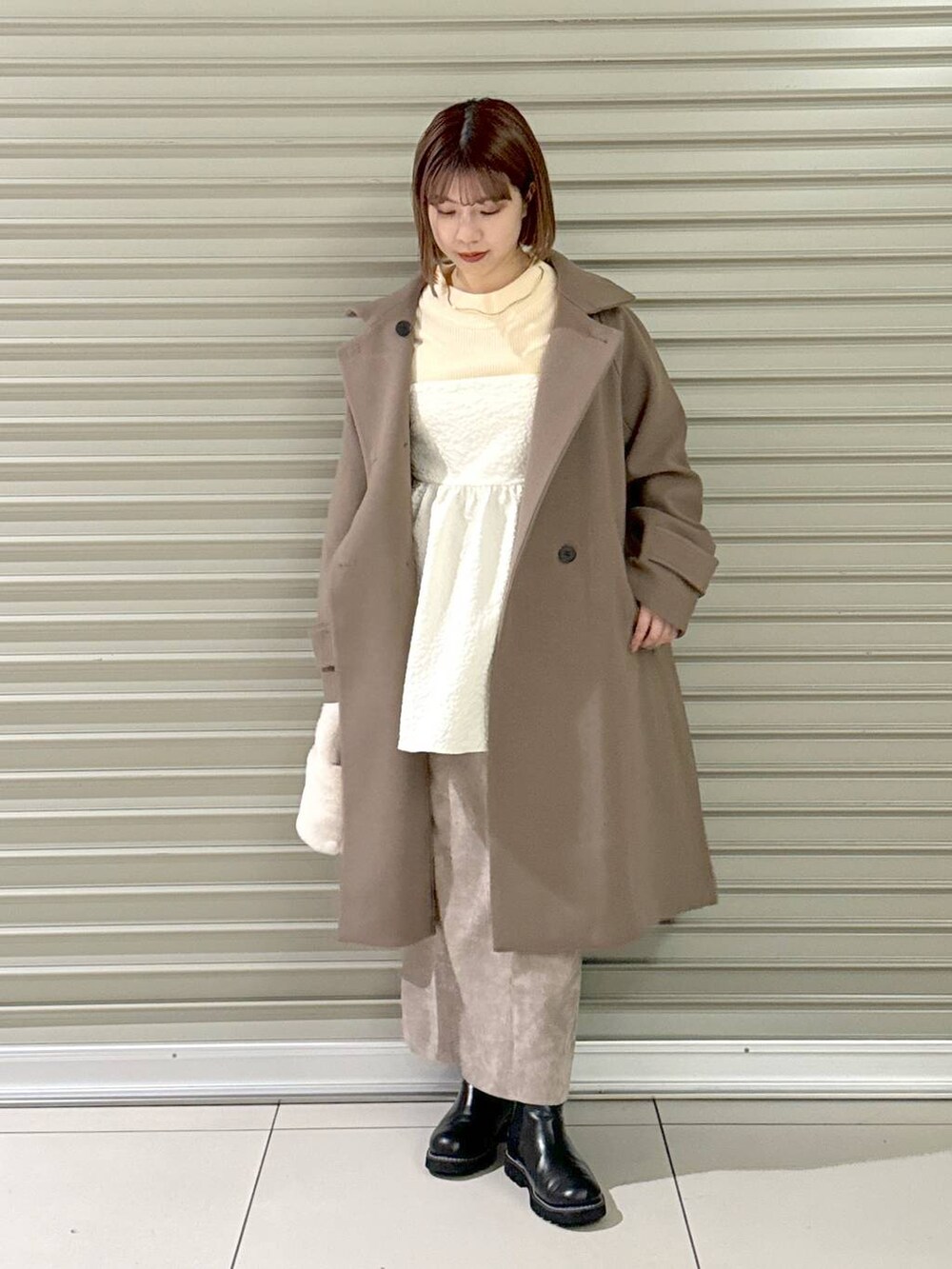 ブラウン系のスカート、ブラウン系のチェスターコート、ホワイト系のキャミソールを着用したレディースの冬コーディネートの2枚目の写真