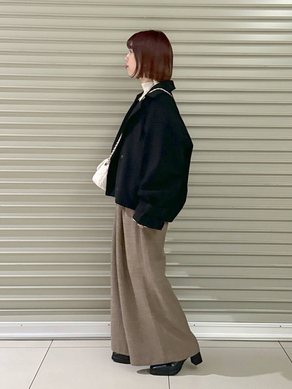 ホワイト系のショルダーバッグ、ブラック系のその他アウター、ブラック系のブーツを着用したレディースの冬コーディネートの2枚目の写真