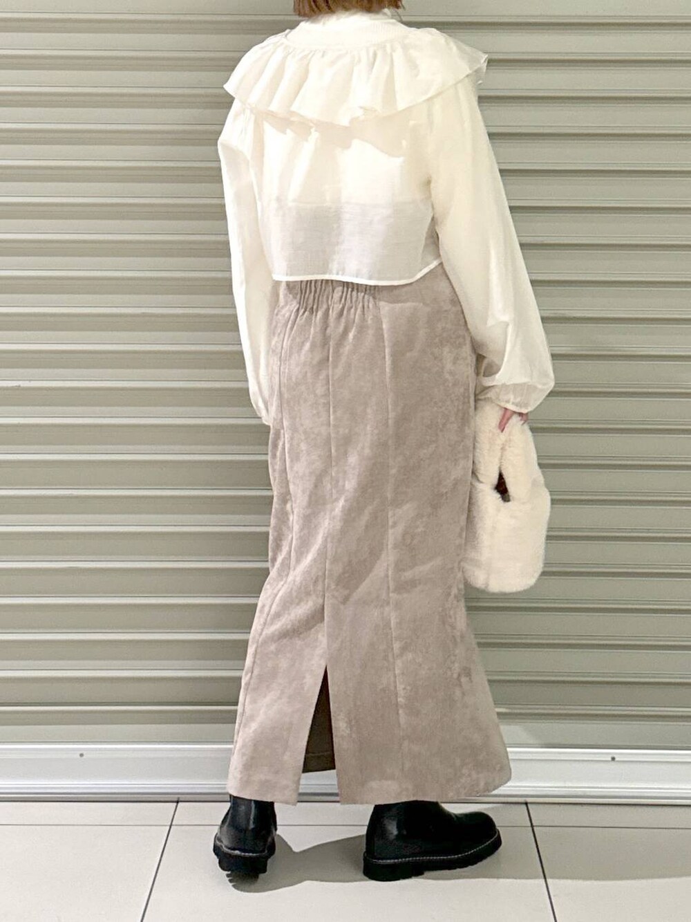 ブラウン系のスカート、ブラック系のブーツ、ホワイト系のハンドバッグを着用したレディースの冬コーディネートの3枚目の写真