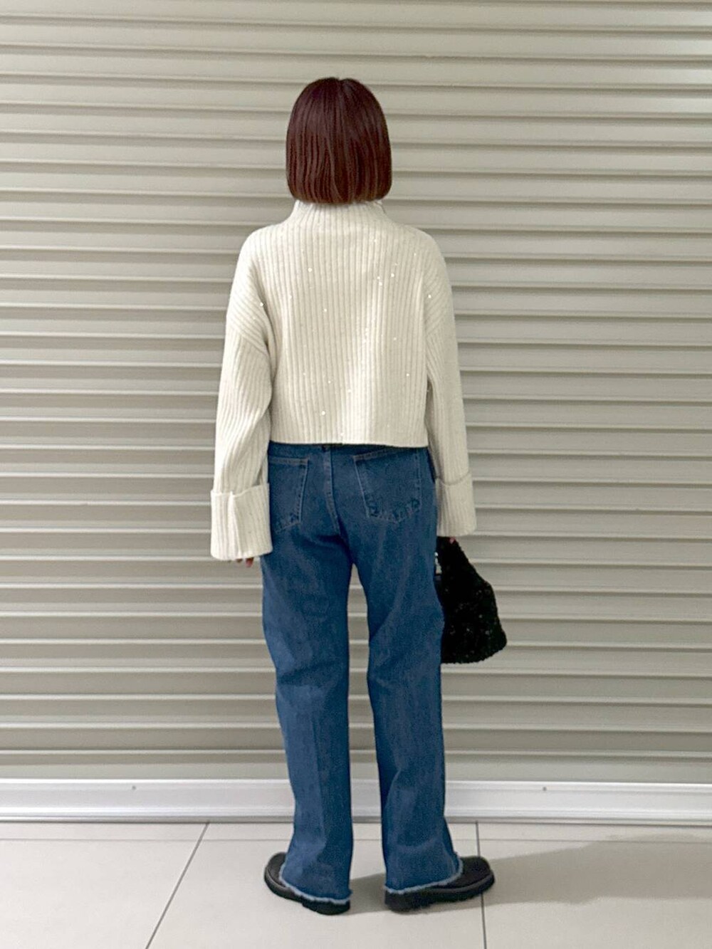 ブルー系のデニムパンツ、ブラック系のブーツ、ブラック系のハンドバッグを着用したレディースの秋コーディネートの3枚目の写真