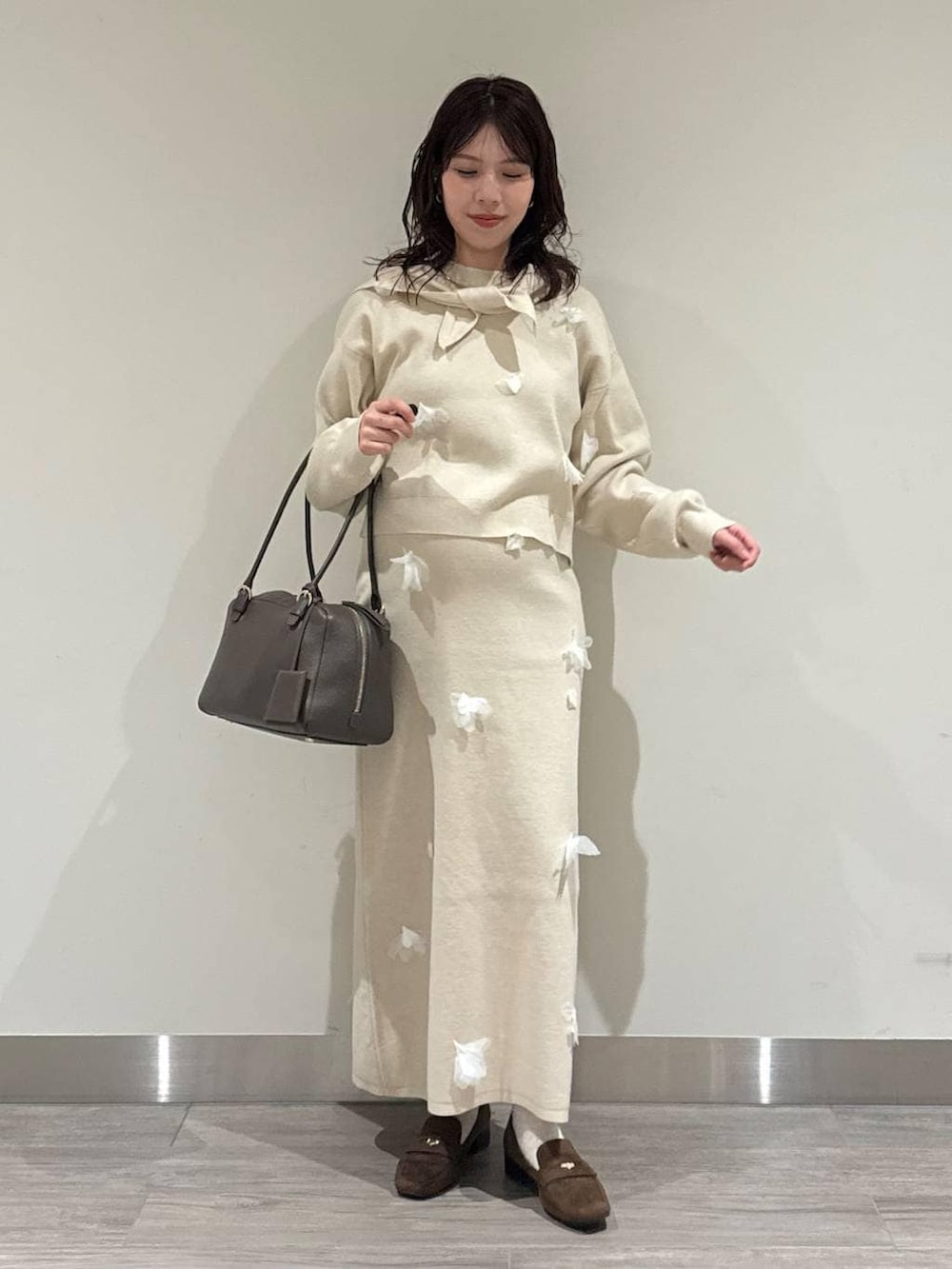 ブラウン系のハンドバッグ、ブラウン系のローファー、ホワイト系のニット/セーターを着用したレディースの冬コーディネートの2枚目の写真