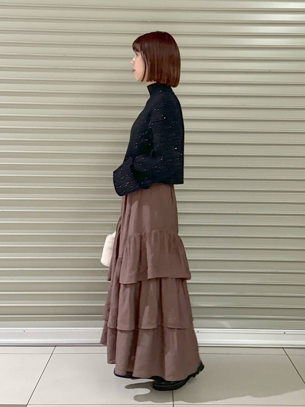 ブラック系のブーツ、ブラウン系のスカート、ホワイト系のハンドバッグを着用したレディースの秋コーディネートの2枚目の写真