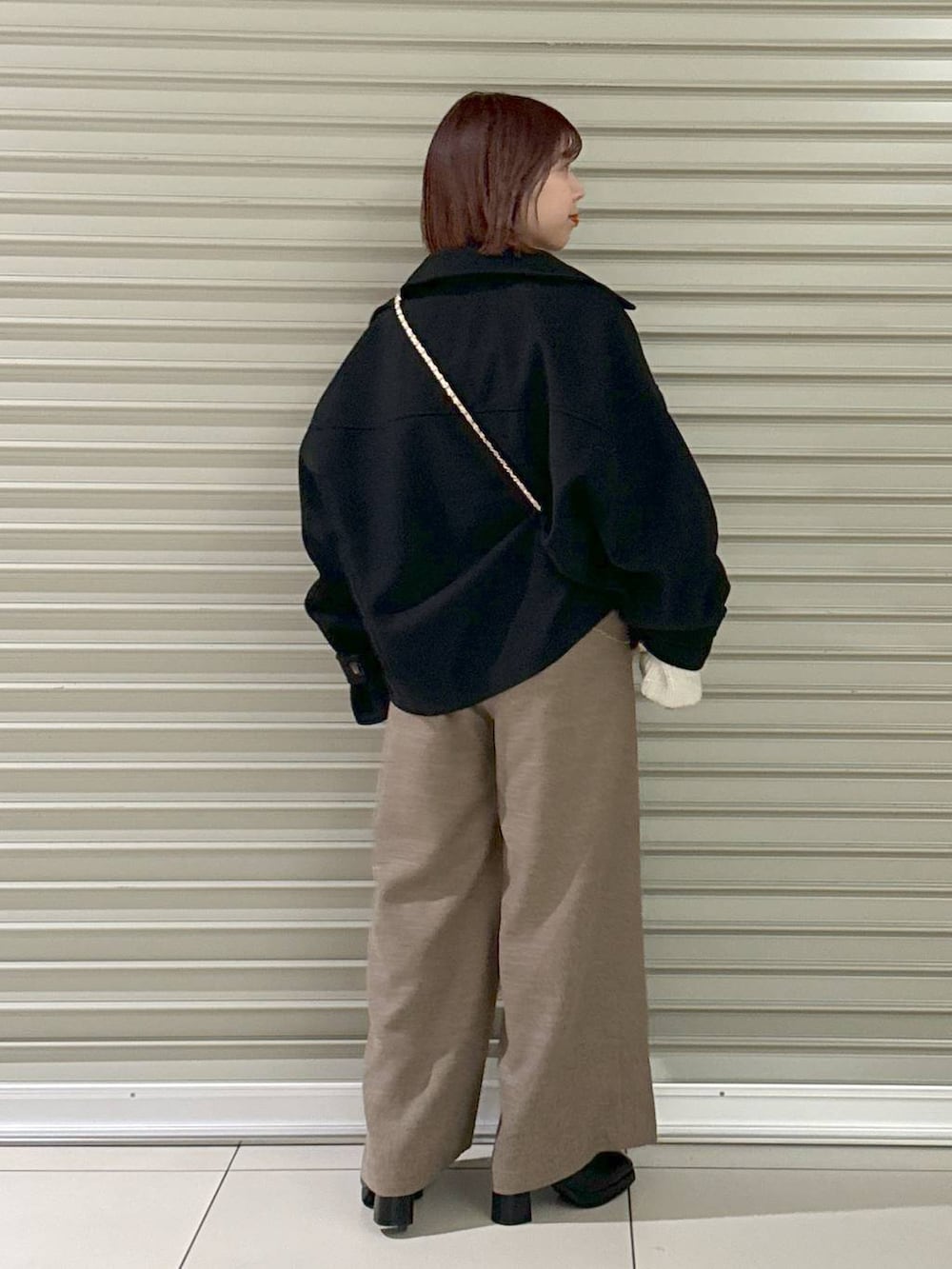 ホワイト系のショルダーバッグ、ブラック系のその他アウター、ブラック系のブーツを着用したレディースの冬コーディネートの3枚目の写真