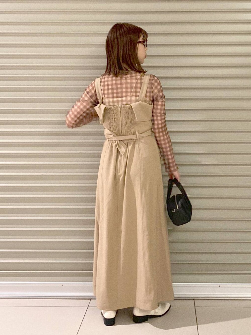 ブラック系のボストンバッグ、ホワイト系のその他シューズ、ベージュ系のジャンパースカートを着用したレディースの夏コーディネートの4枚目の写真