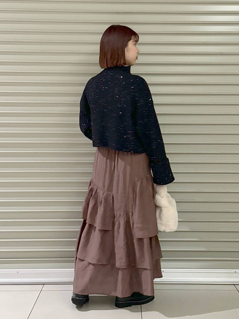 ブラック系のブーツ、ブラウン系のスカート、ホワイト系のハンドバッグを着用したレディースの秋コーディネートの3枚目の写真