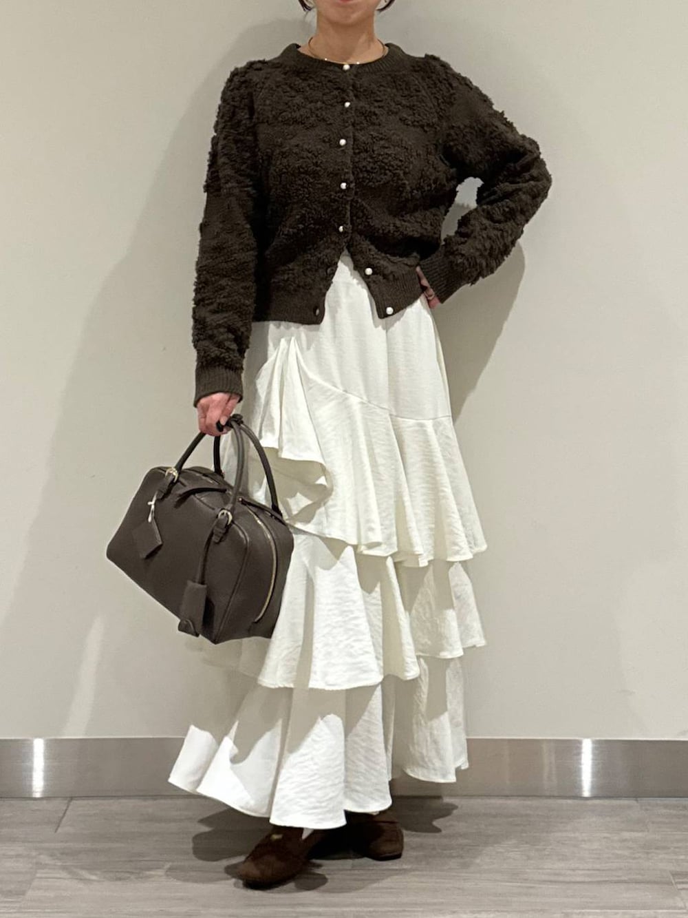 ブラウン系のハンドバッグ、ブラウン系のカーディガン/ボレロ、ホワイト系のスカートを着用したレディースの秋コーディネートの2枚目の写真