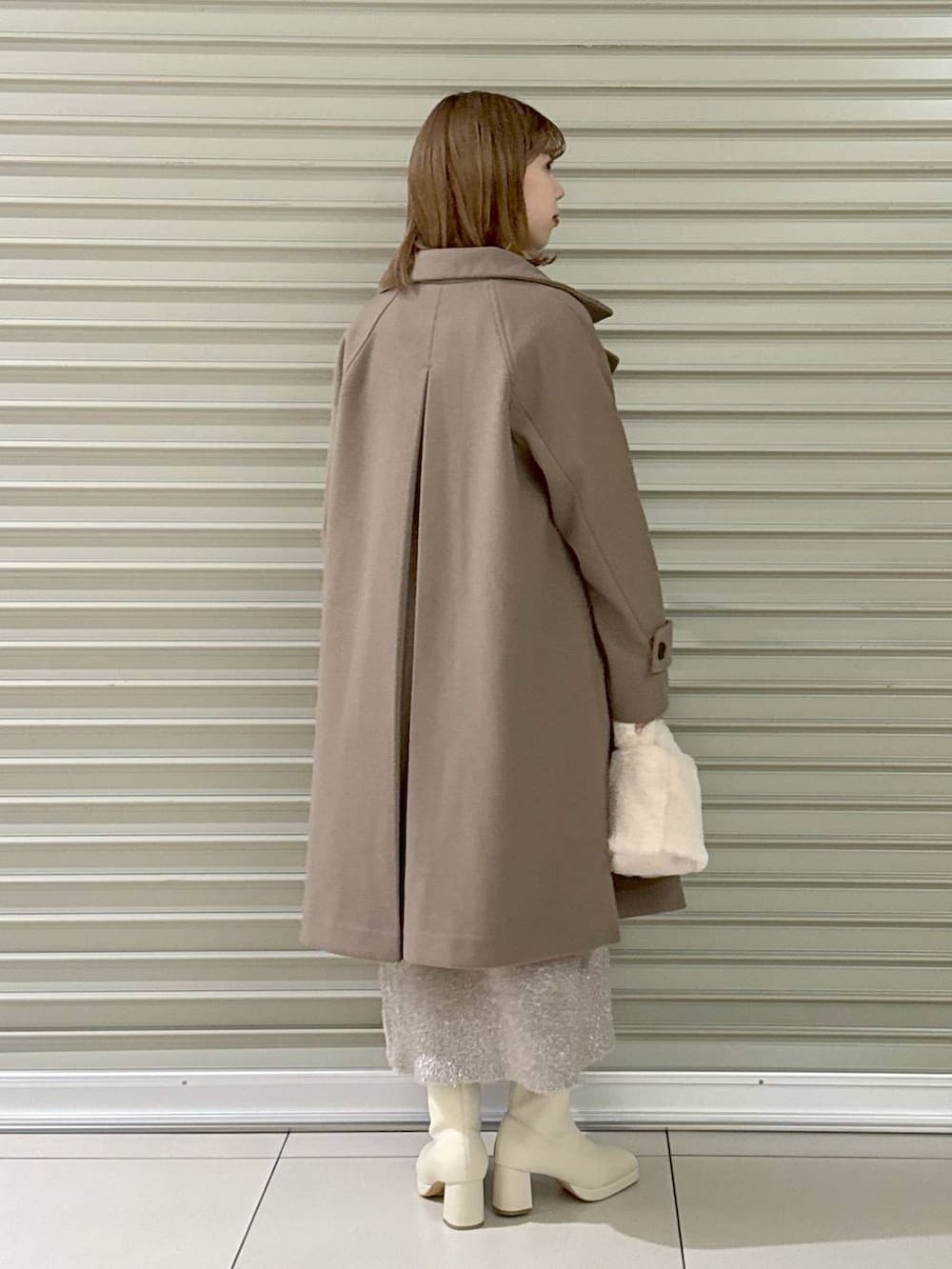 ブラウン系のチェスターコート、ホワイト系のブーツ、ホワイト系のハンドバッグを着用したレディースの冬コーディネートの2枚目の写真