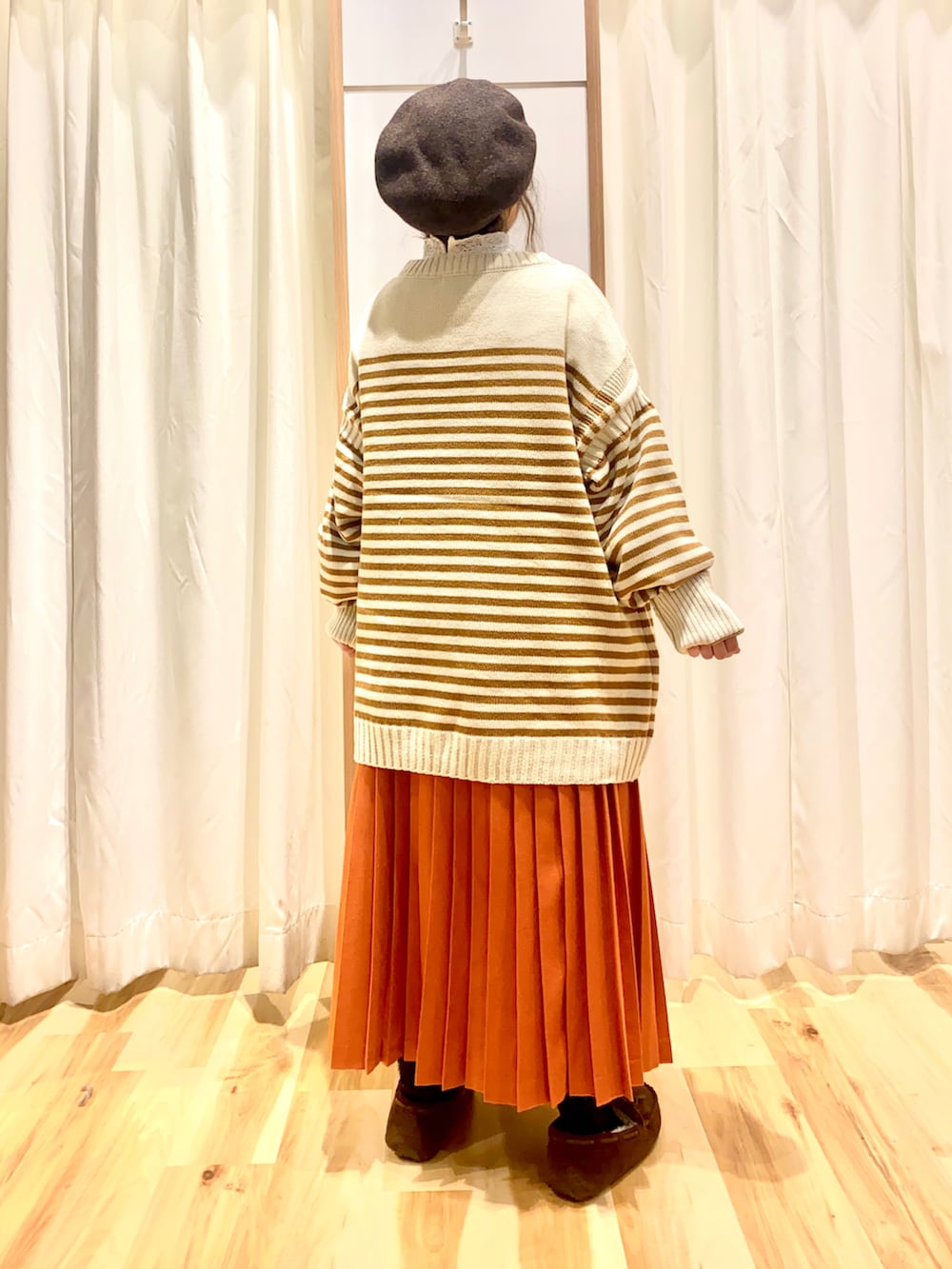 イエロー系のニット/セーター、オレンジ系のスカート、ブラウン系のモカシン/デッキシューズを着用したレディースの冬コーディネートの2枚目の写真