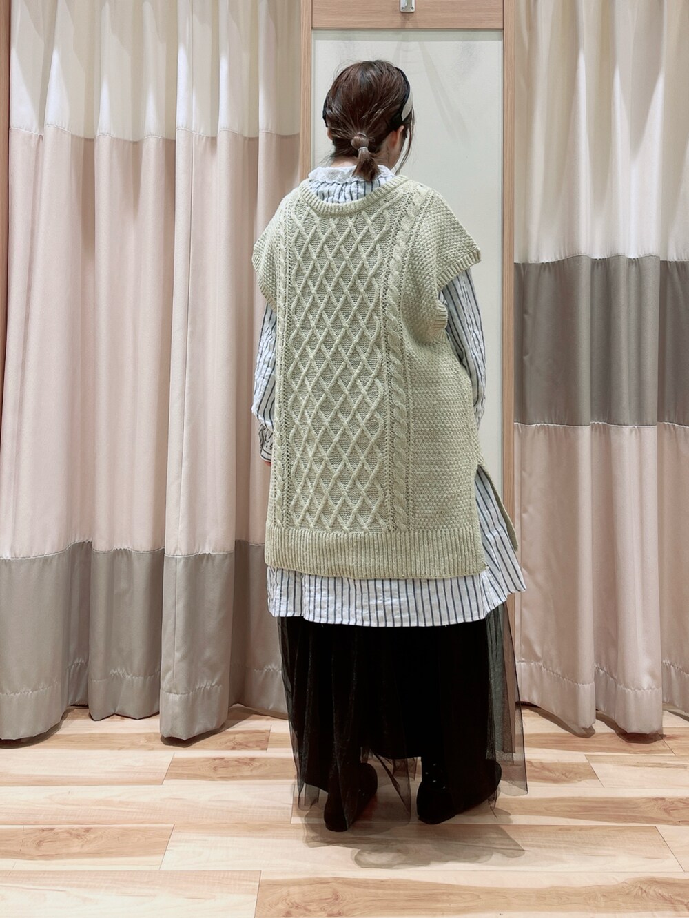 グリーン系のベスト、ブルー系のチュニック、ブラック系のスカートを着用したレディースの冬コーディネートの2枚目の写真