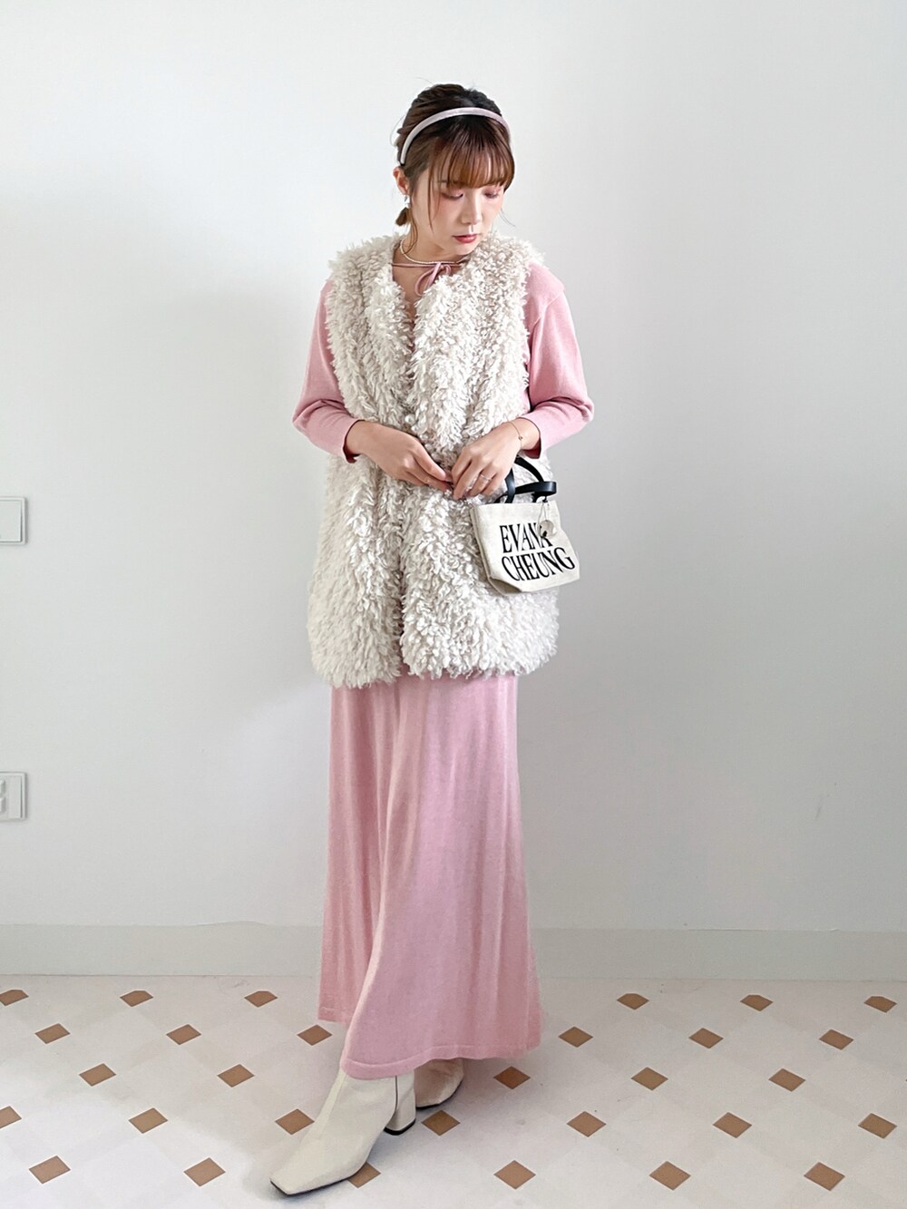 ホワイト系のベスト、ピンク系のワンピース、ブラウン系のブーツを着用したレディースの冬コーディネートの2枚目の写真