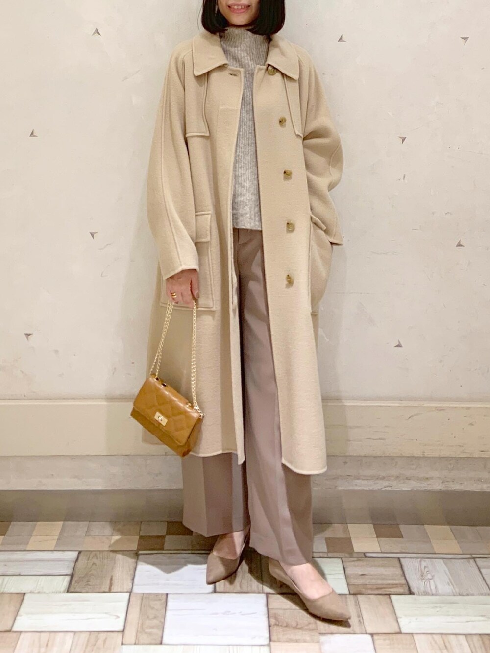 イエロー系のステンカラーコート、ベージュ系のニット/セーター、イエロー系のショルダーバッグを着用したレディースの冬コーディネートの3枚目の写真