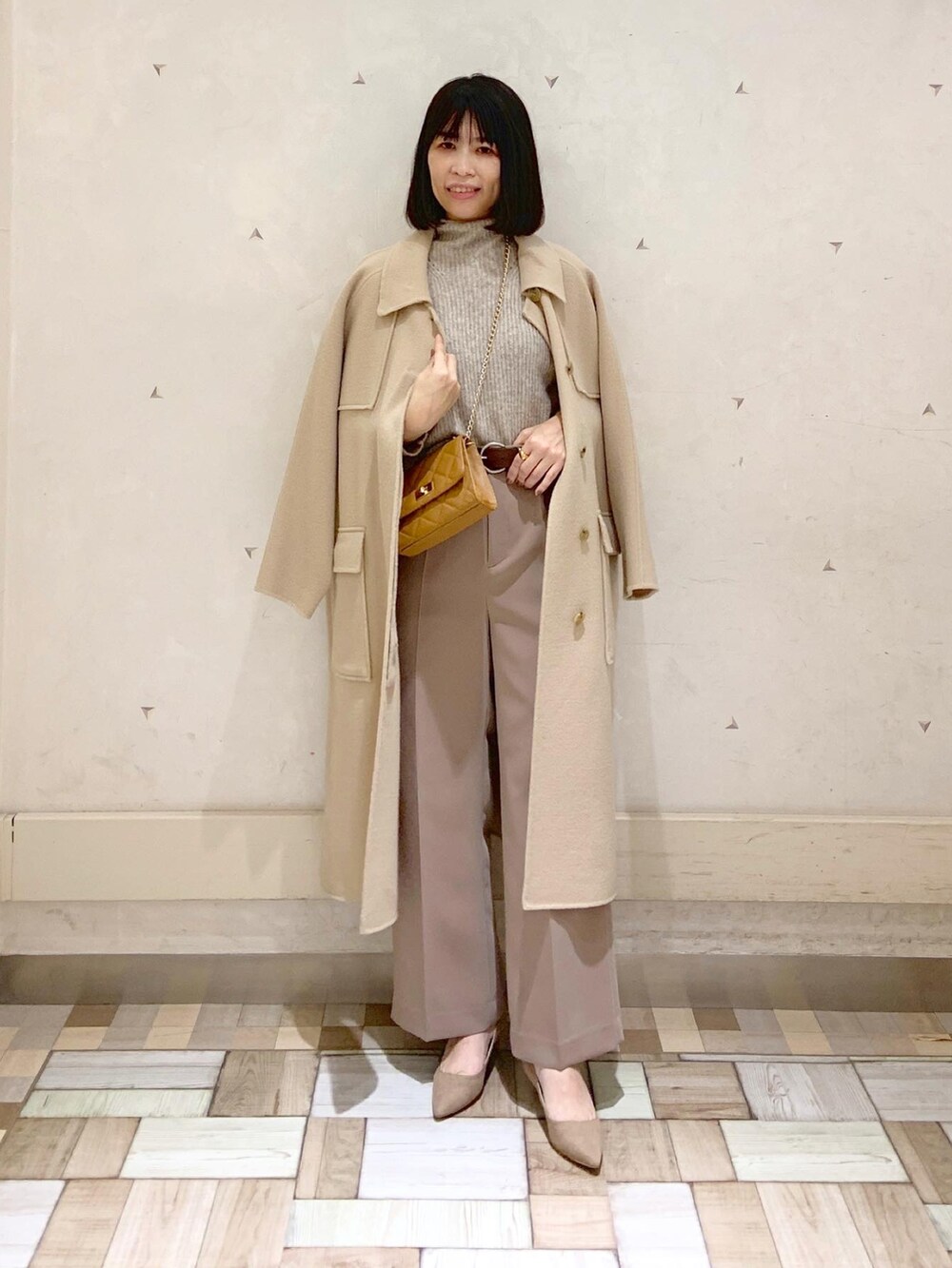 イエロー系のステンカラーコート、ベージュ系のニット/セーター、イエロー系のショルダーバッグを着用したレディースの冬コーディネートの5枚目の写真