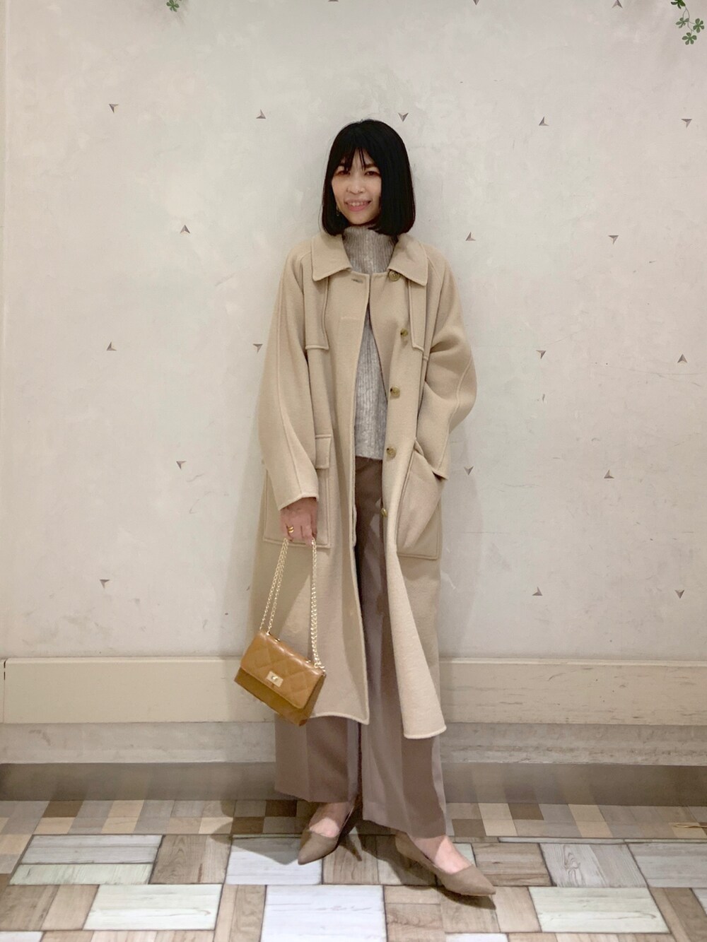 イエロー系のステンカラーコート、ベージュ系のニット/セーター、イエロー系のショルダーバッグを着用したレディースの冬コーディネートの2枚目の写真