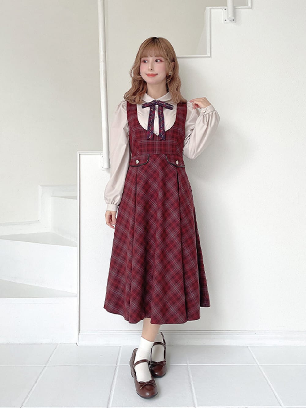 レッド系のジャンパースカート、ブラウン系のバレエシューズ、ベージュ系のシャツ/ブラウスを着用したレディースの冬コーディネートの2枚目の写真