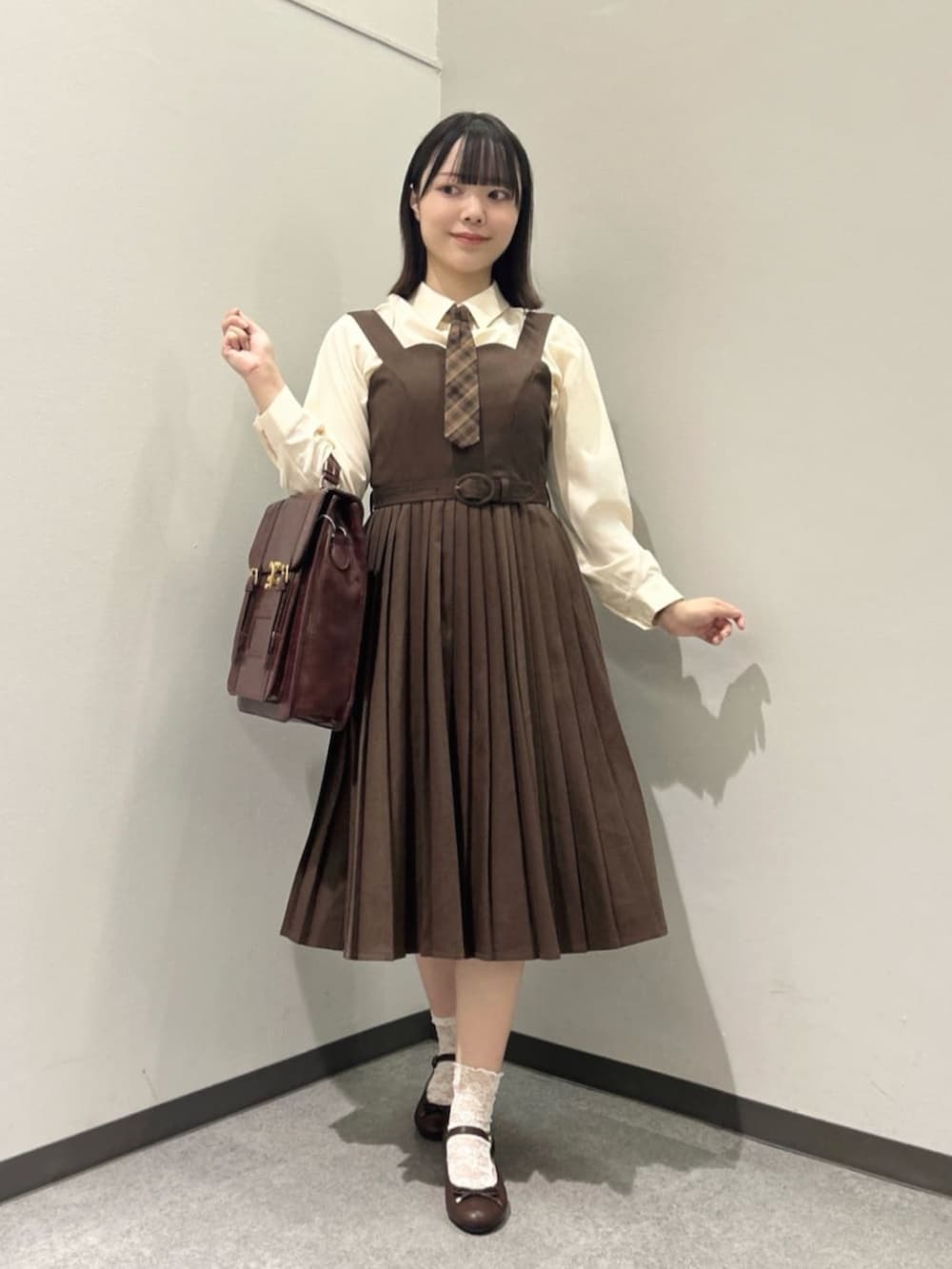 ブラウン系のハンドバッグ、ブラウン系のジャンパースカート、ベージュ系のシャツ/ブラウスを着用したレディースの秋コーディネートの2枚目の写真