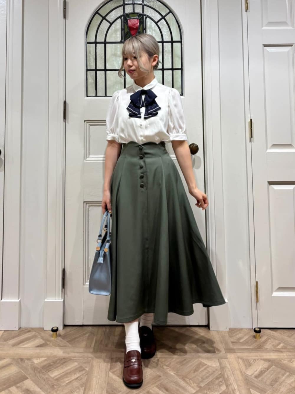 ブラウン系のローファー、ホワイト系のシャツ/ブラウス、グリーン系のスカートを着用したレディースの夏コーディネートの2枚目の写真