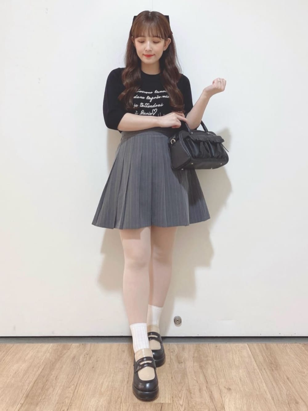 グレー系のスカート、ブラック系のハンドバッグ、ブラック系のローファーを着用したレディースの秋コーディネートの2枚目の写真