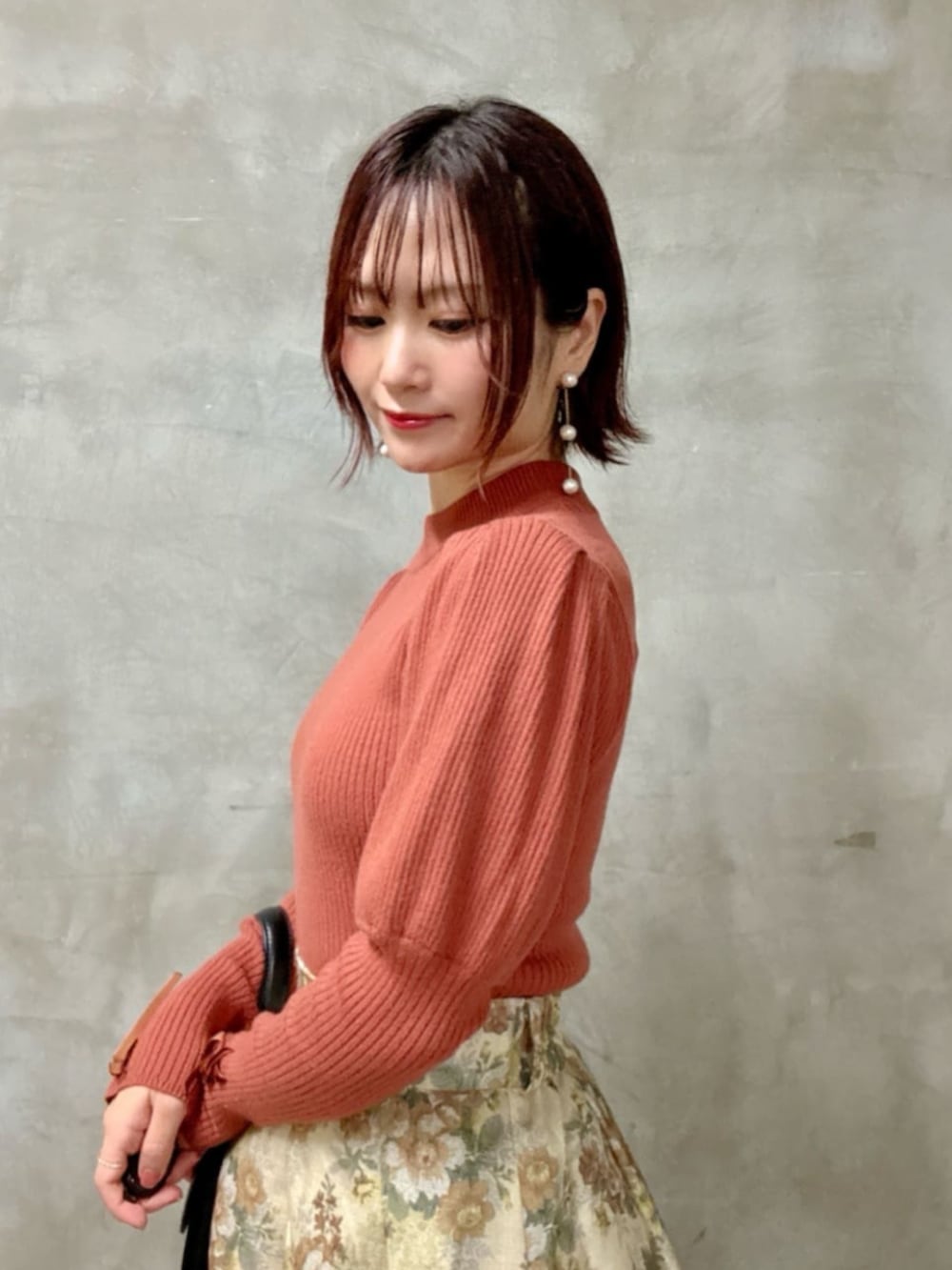 ブラック系のハンドバッグ、ベージュ系のスカート、オレンジ系のニット/セーターを着用したレディースの秋コーディネートの2枚目の写真