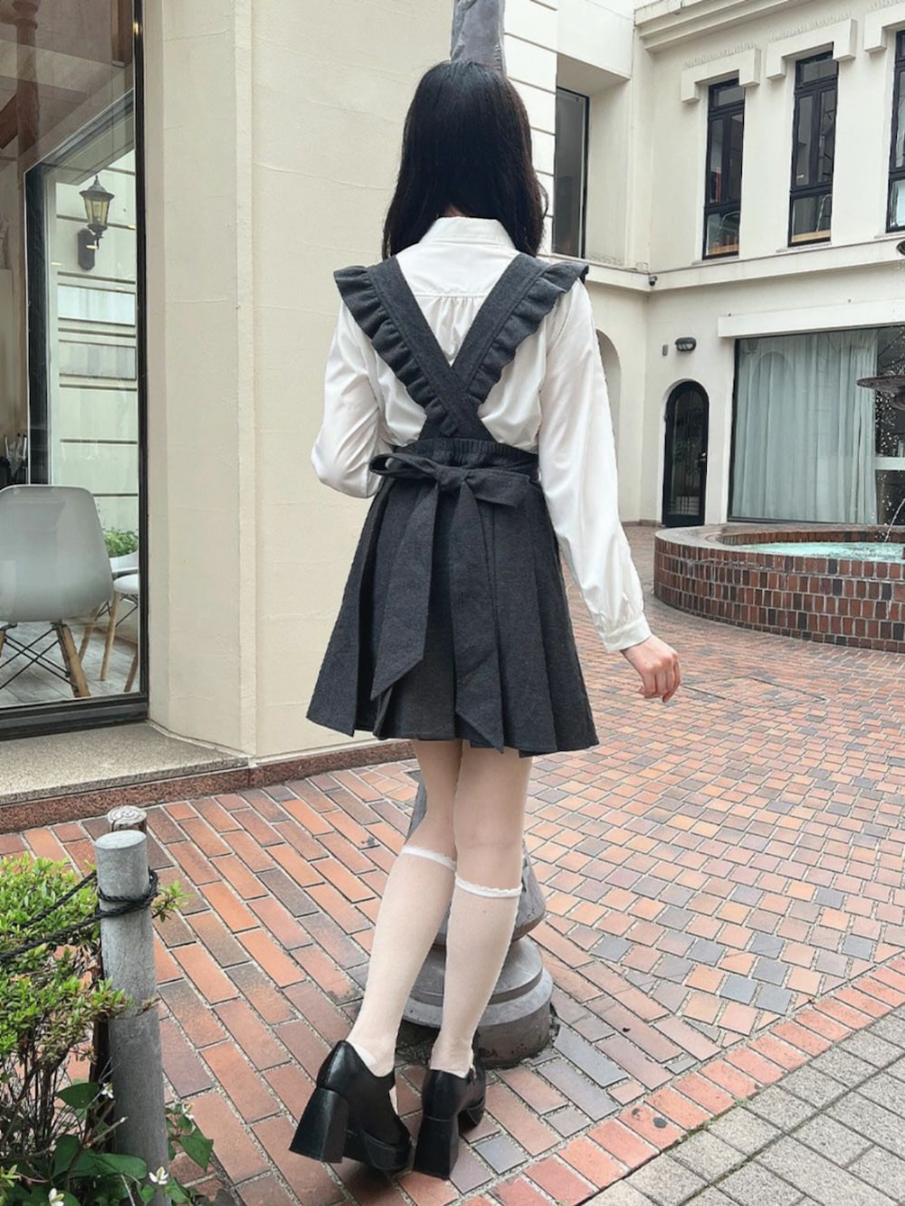 ブラック系のパンプス、グレー系のジャンパースカート、ホワイト系のシャツ/ブラウスを着用したレディースの秋コーディネートの3枚目の写真