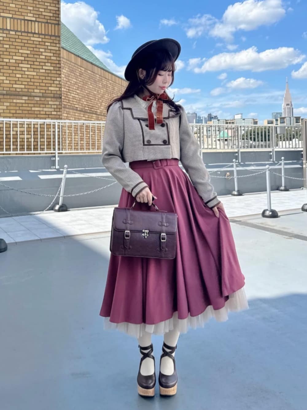 ピンク系のスカート、ブラウン系のショルダーバッグ、ブラウン系のパンプスを着用したレディースの秋コーディネートの2枚目の写真