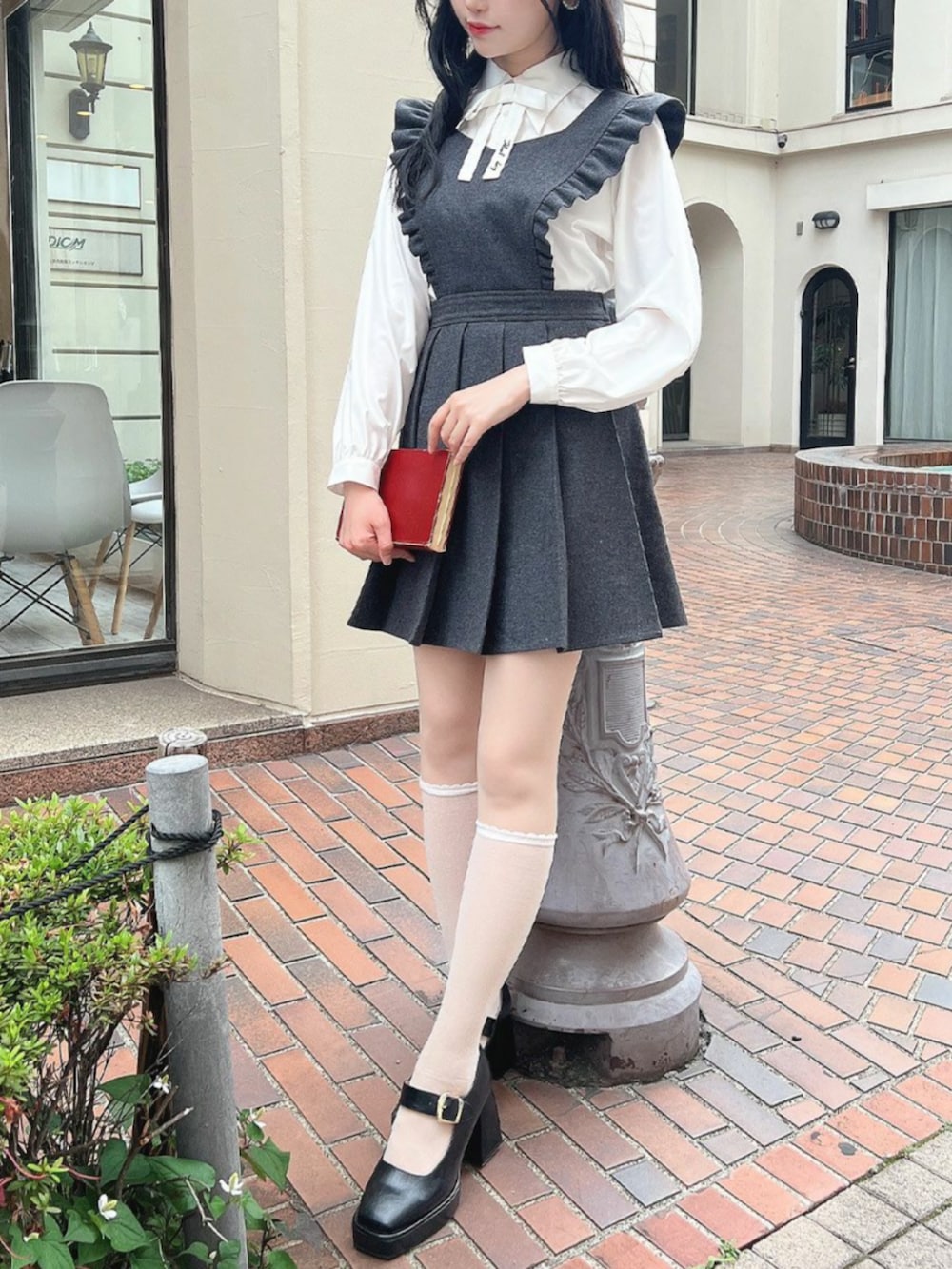 ブラック系のパンプス、グレー系のジャンパースカート、ホワイト系のシャツ/ブラウスを着用したレディースの秋コーディネートの2枚目の写真