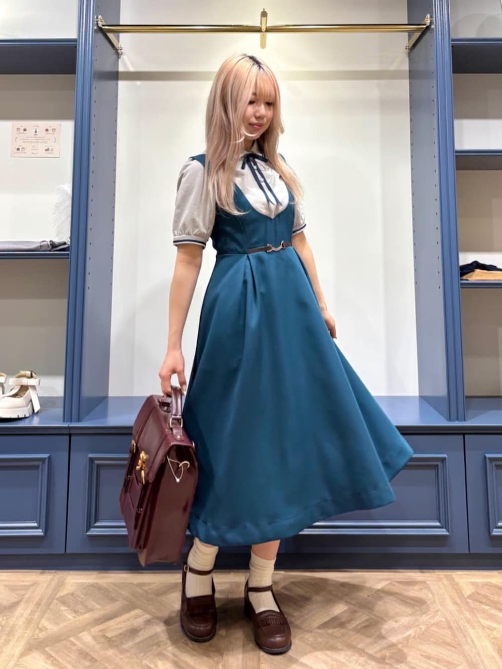 ブラウン系のハンドバッグ、ブラウン系のローファー、ブルー系のジャンパースカートを着用したレディースの夏コーディネートの2枚目の写真