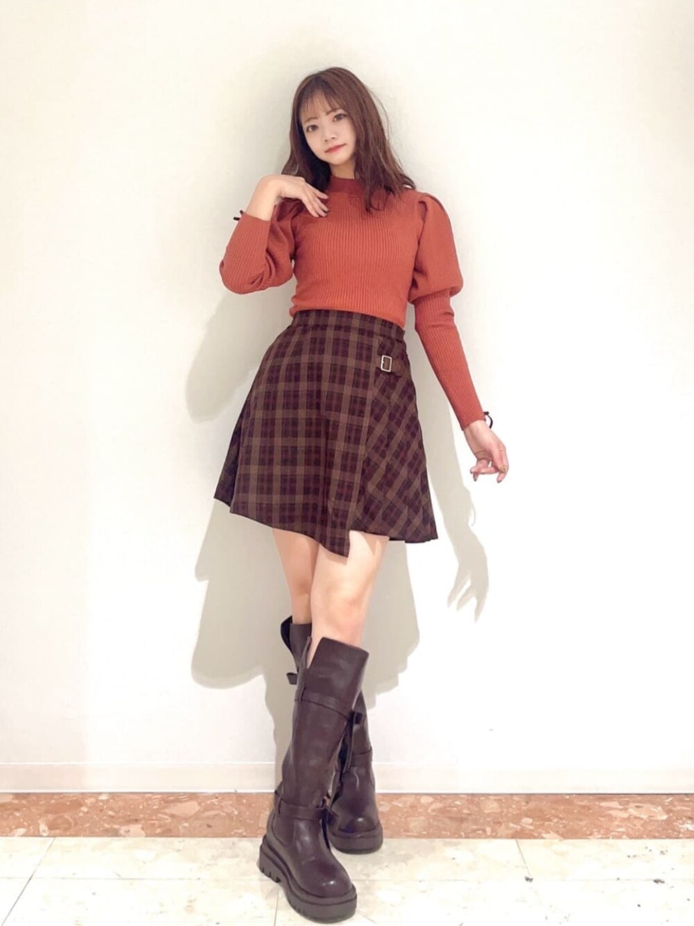 ブラウン系のブーツ、ブラウン系のスカート、オレンジ系のニット/セーターを着用したレディースの秋コーディネートの2枚目の写真