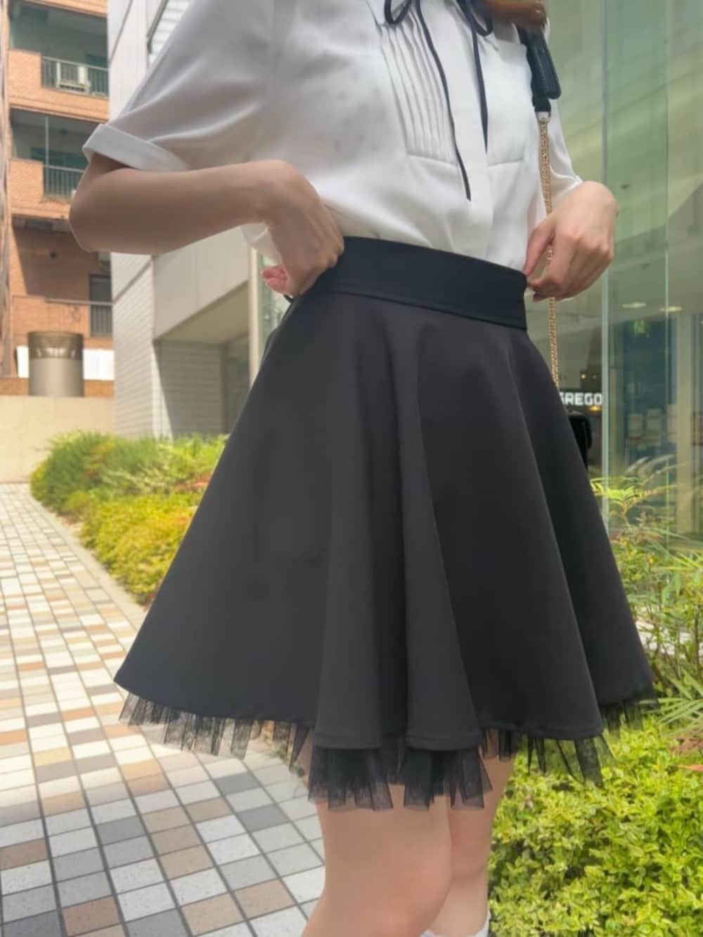 ブラック系のスカート、ブラック系のサンダル、ホワイト系のシャツ/ブラウスを着用したレディースの春コーディネートの2枚目の写真