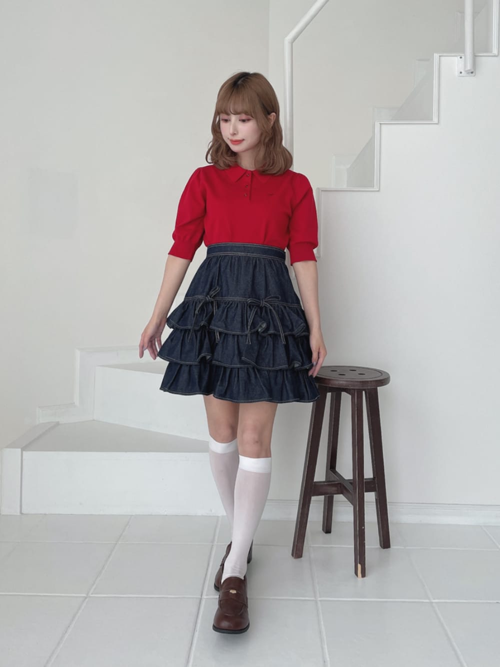 レッド系のポロシャツ、ブラウン系のローファー、ブルー系のスカートを着用したレディースの夏コーディネートの3枚目の写真