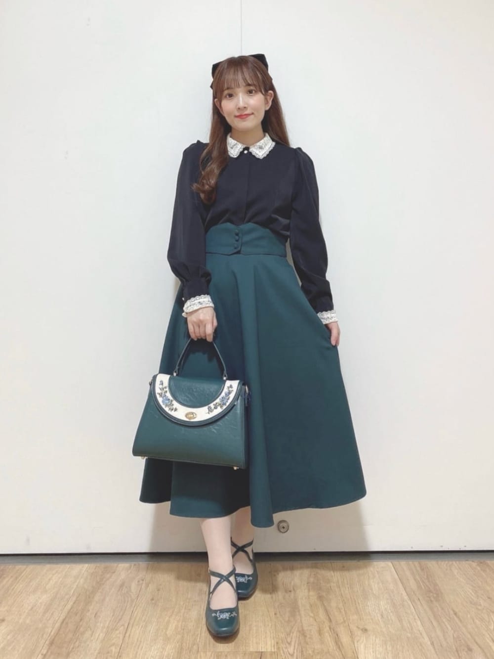 ブルー系のハンドバッグ、ブルー系のパンプス、グリーン系のスカートを着用したレディースの秋コーディネートの2枚目の写真