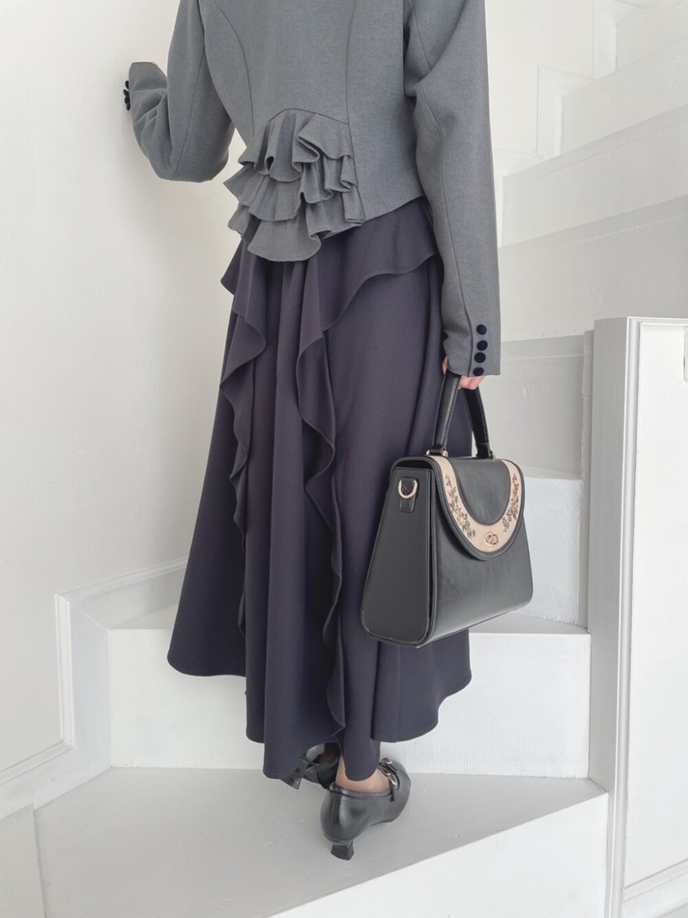 ブラック系のパンプス、ブラック系のハンドバッグ、グレー系のテーラードジャケットを着用したレディースの秋コーディネートの3枚目の写真