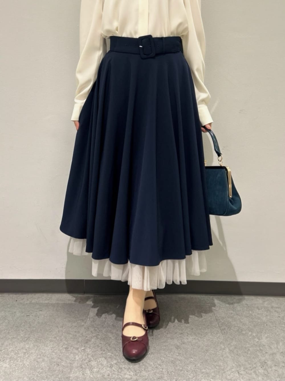 ブルー系のスカート、ブルー系のハンドバッグ、レッド系のパンプスを着用したレディースの秋コーディネートの3枚目の写真