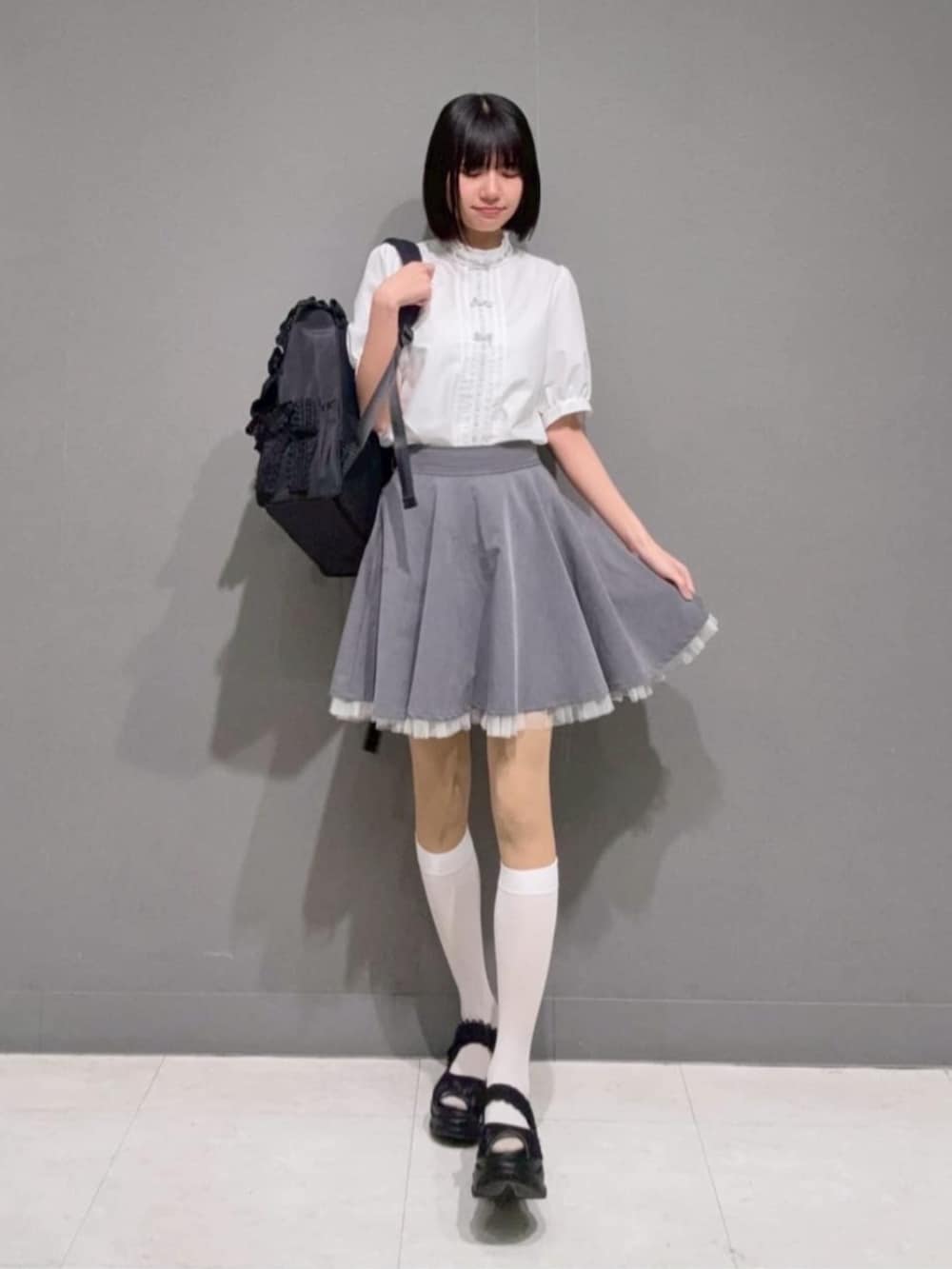 グレー系のスカート、ホワイト系のシャツ/ブラウス、ブラック系のサンダルを着用したレディースの春コーディネートの2枚目の写真