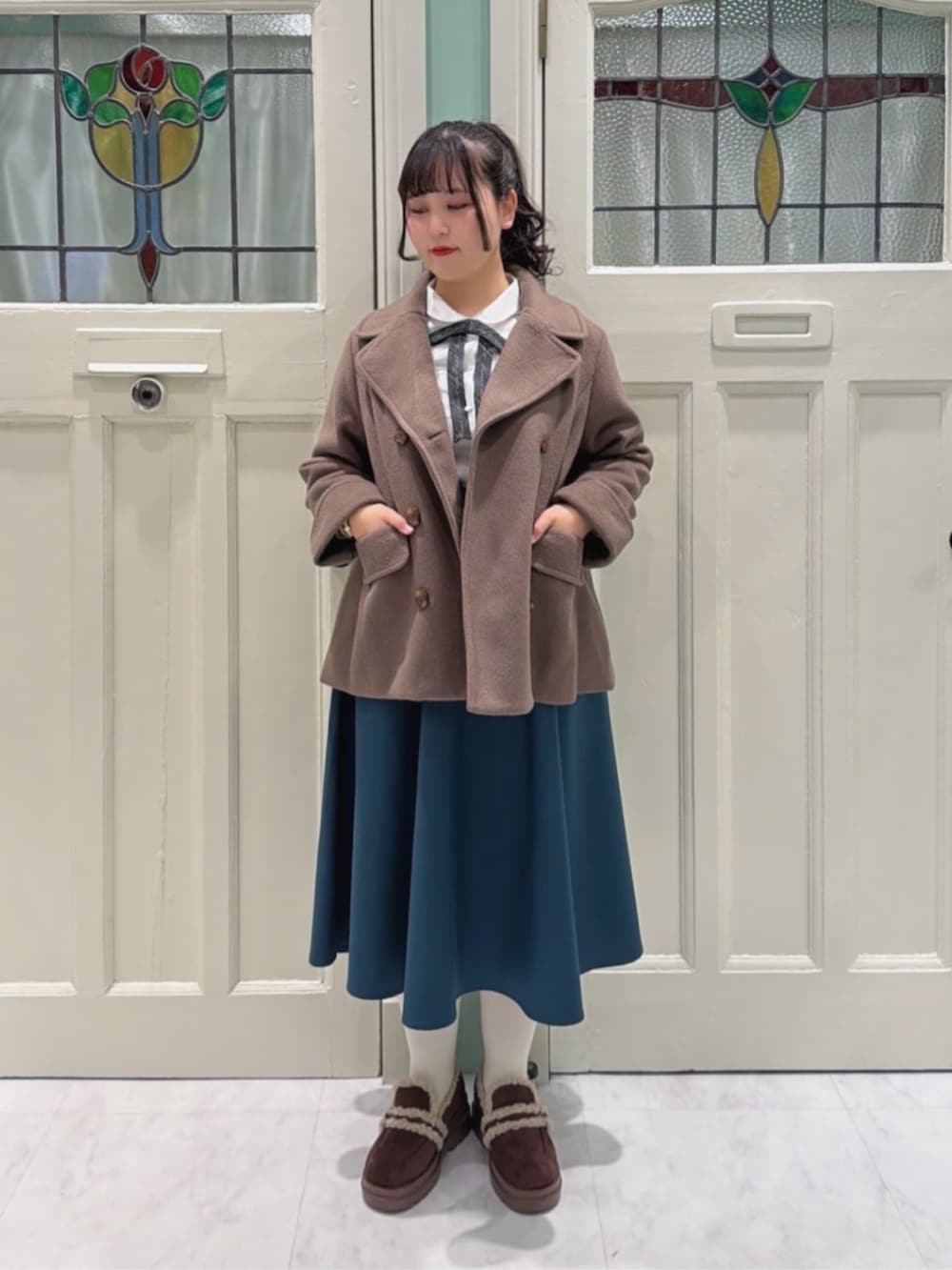 ブルー系のショルダーバッグ、ブラウン系のピーコート、ホワイト系のシャツ/ブラウスを着用したレディースの冬コーディネートの2枚目の写真