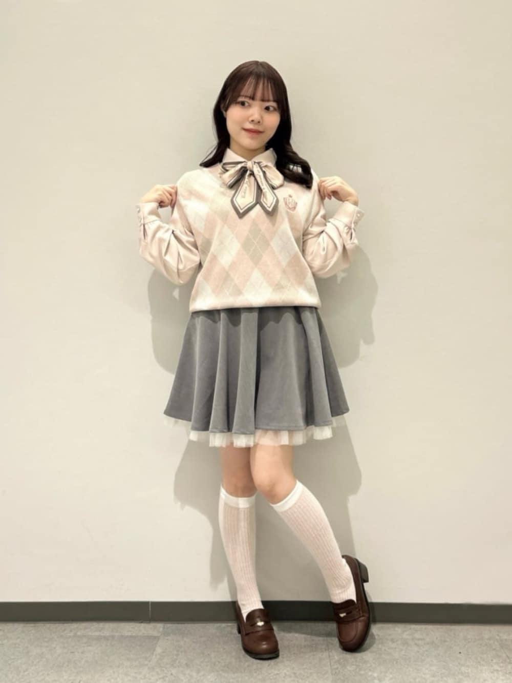 グレー系のスカート、ブラウン系のローファー、ピンク系のベストを着用したレディースの春コーディネートの2枚目の写真