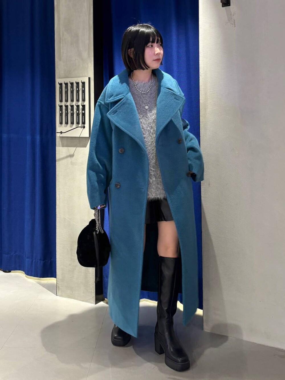 グリーン系のチェスターコート、ブラック系のブーツ、グレー系のニット/セーターを着用したレディースの冬コーディネートの2枚目の写真